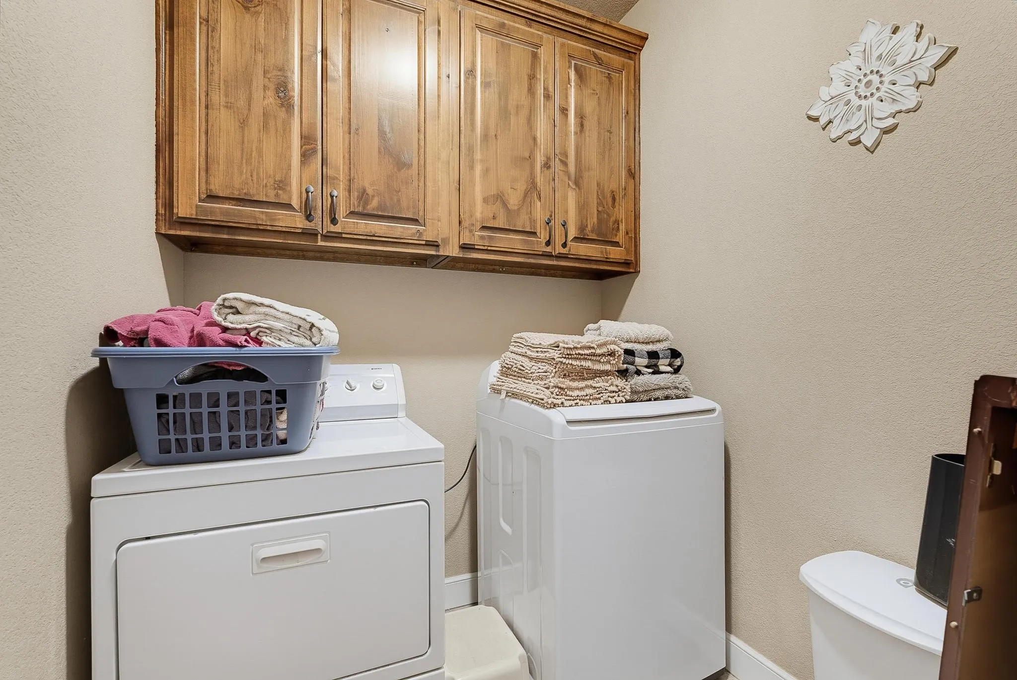 Laundry area featuring overhead wood cabinetry with dark hardware and light-toned walls