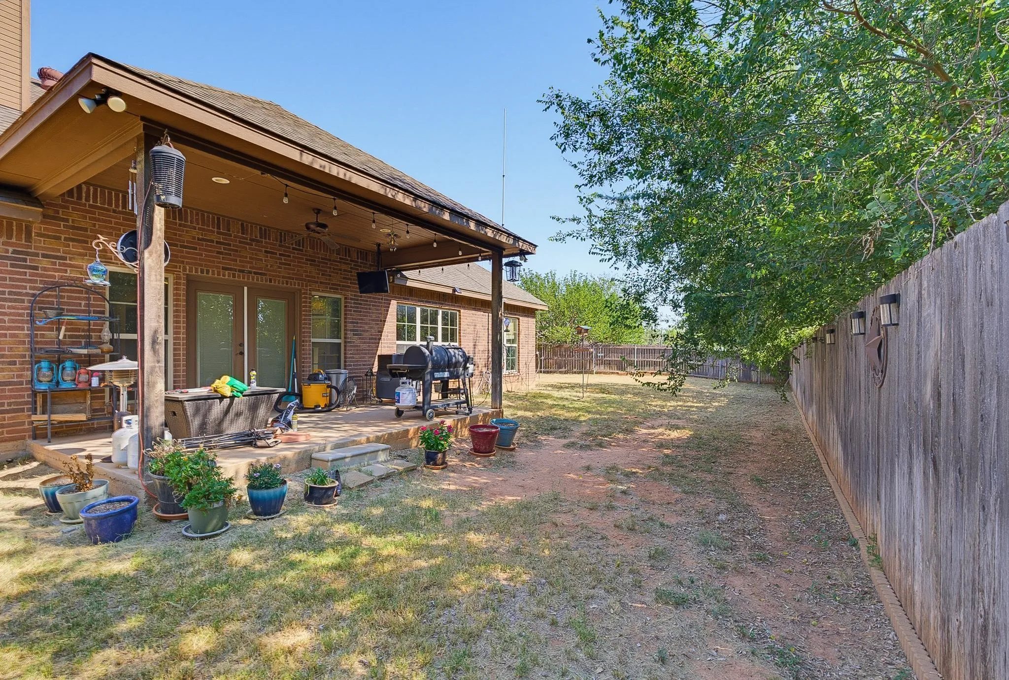 Expansive backyard featuring a covered patio, brick exterior, wood fence, and mature trees