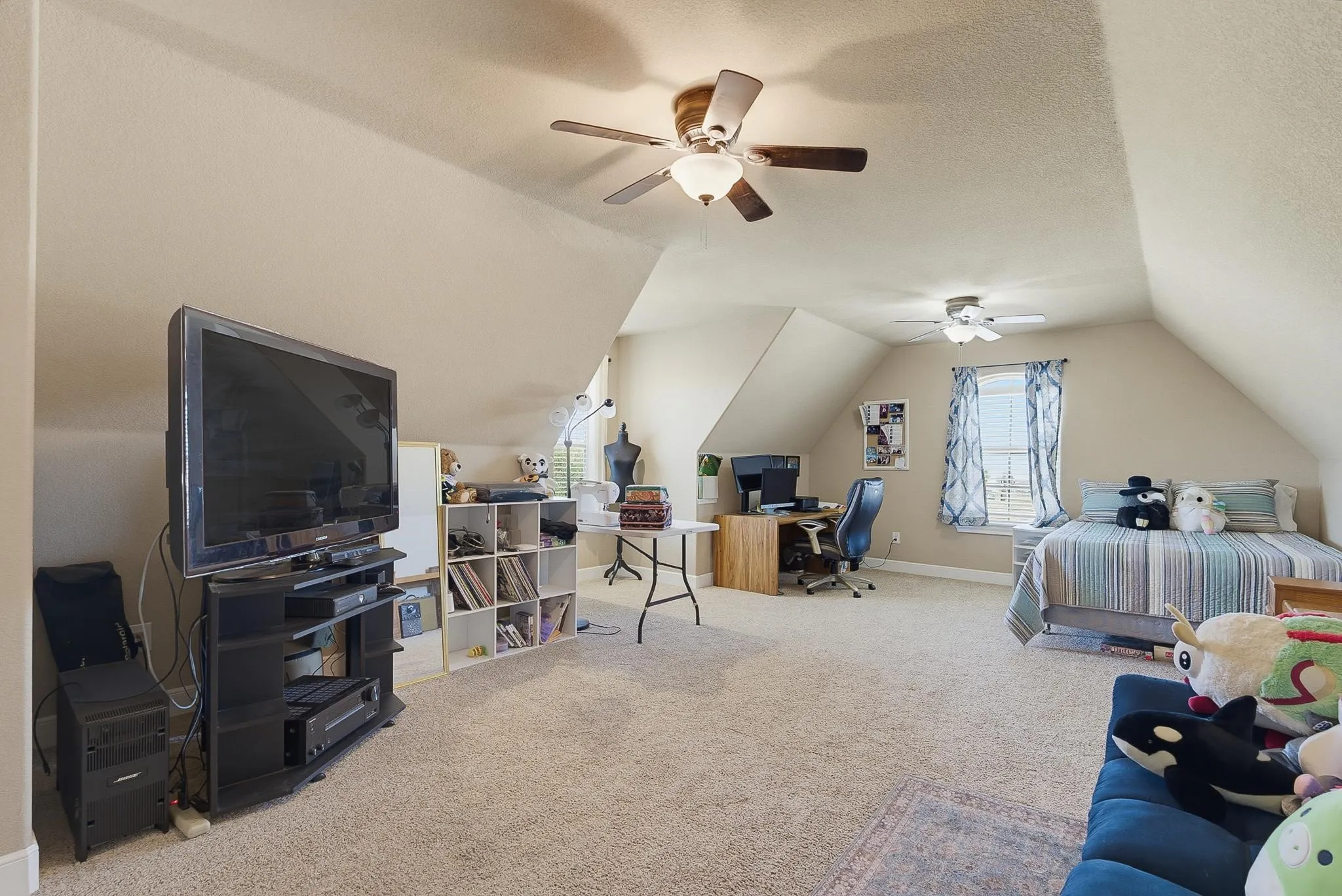 Expansive room featuring sloped ceilings, two ceiling fans with integrated lighting, window with drapes, and carpet flooring