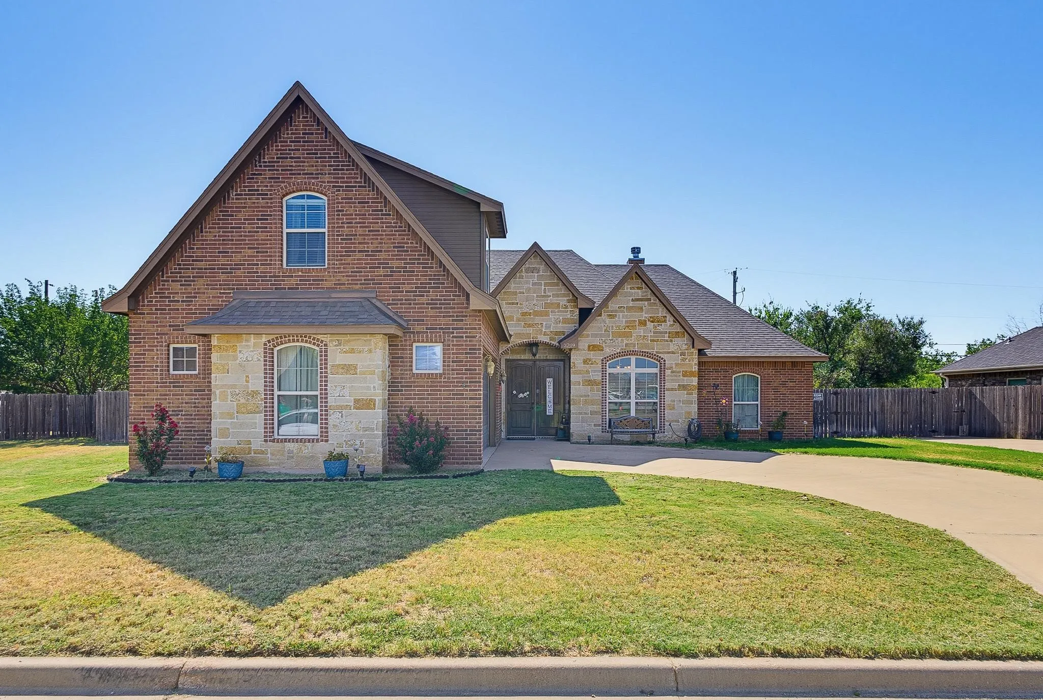 Brick and stone exterior featuring varied rooflines, an arched window, and a concrete driveway
