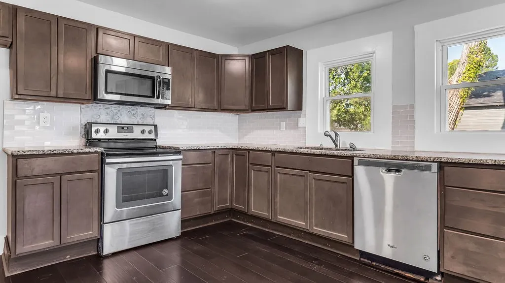Corner kitchen featuring dark wood-finish cabinetry, speckled countertops, and stainless steel appliances including a microwave, range, and dishwasher