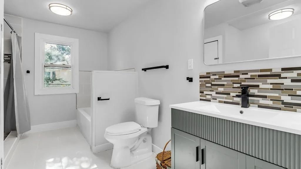 2nd/hall Contemporary bathroom featuring a stylish vanity with a fluted panel front, a sleek rectangular mirror, and a mosaic tile backsplash