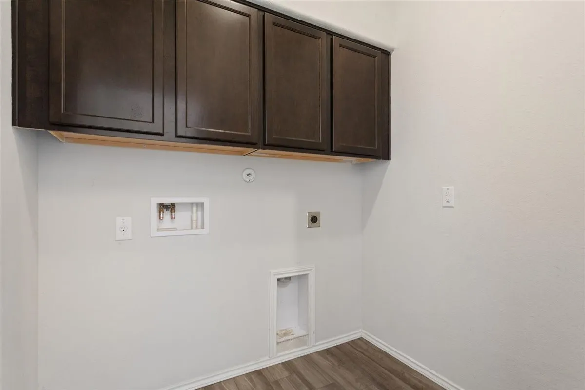 Dedicated utility space with dark wood-finish cabinetry, light gray walls, and wood-finish flooring