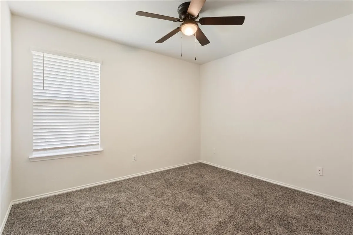 Neutral-toned room featuring a window with white blinds, a ceiling fan with integrated lighting, and plush carpet flooring