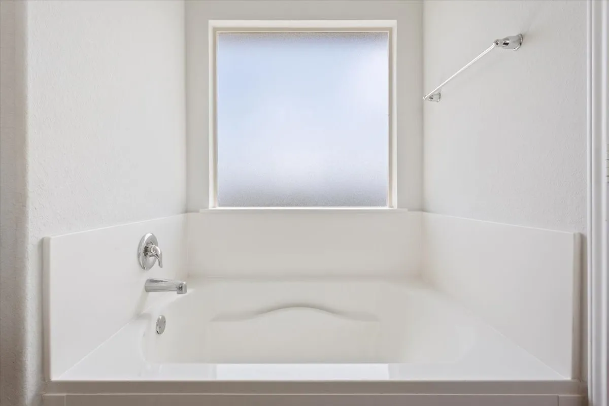 Built-in soaking tub with chrome fixtures, a frosted window, and a wall-mounted towel bar