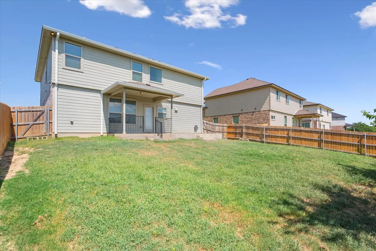 Spacious backyard featuring a covered patio with metal railings, a full privacy fence, and a two-story exterior with siding and brick accents