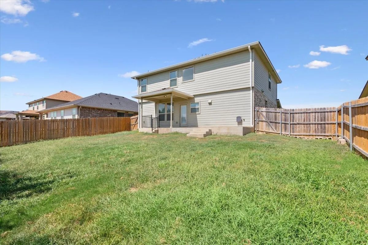 Expansive backyard featuring a covered patio with railing, privacy fencing, and a two-story exterior with siding and stone accents