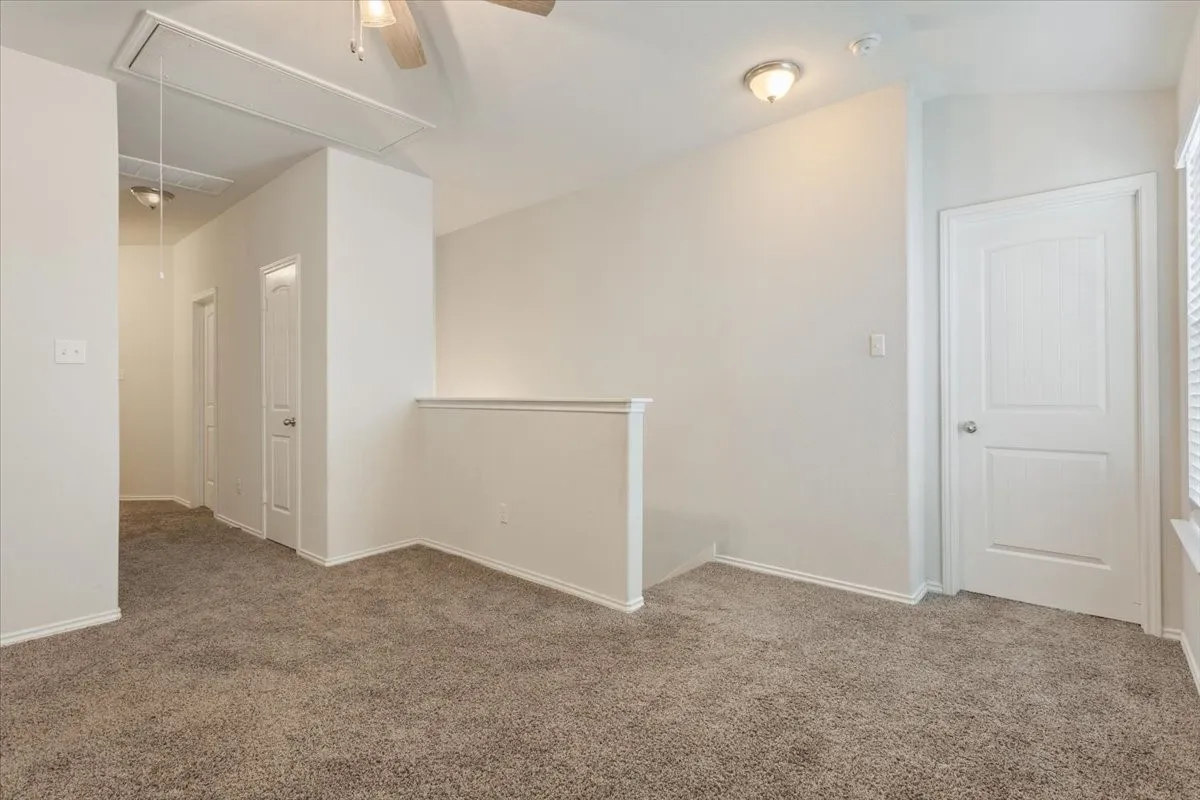 Carpeted loft area featuring a ceiling fan, pull-down attic access, a white paneled door, and a semi-flush mount light fixture