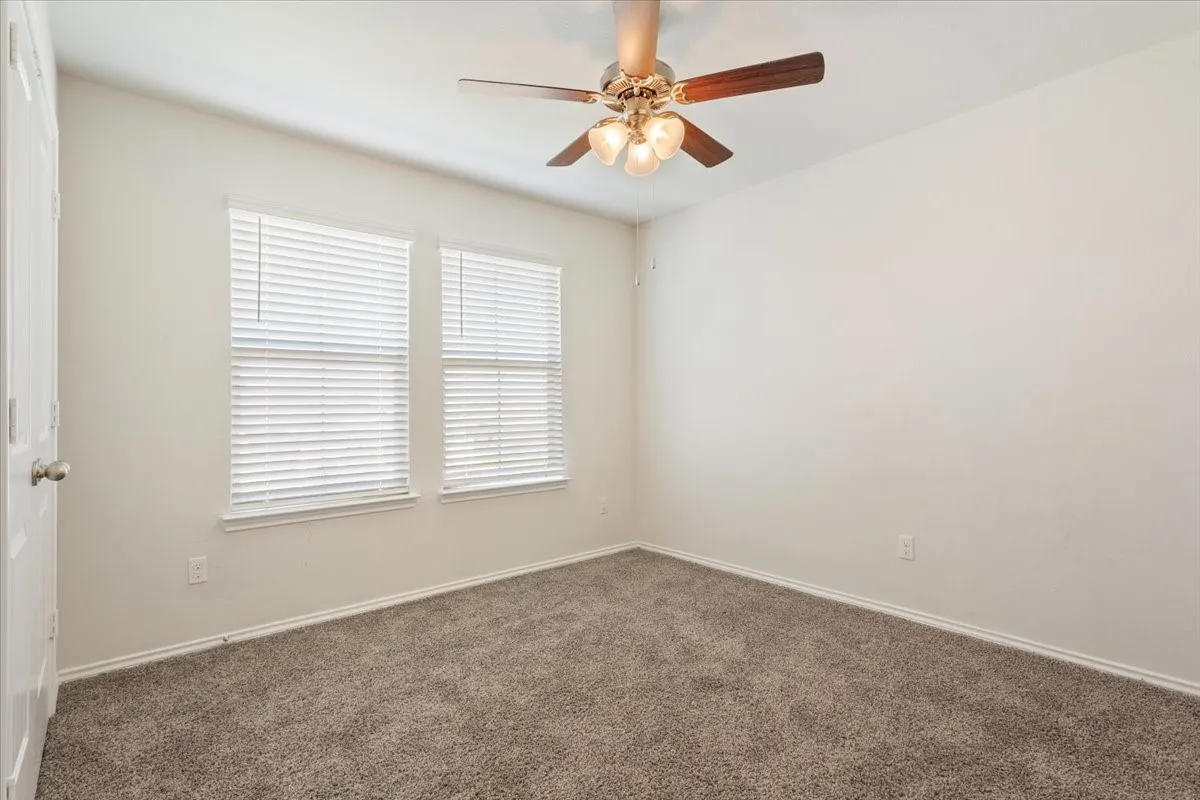Carpeted room featuring a ceiling fan with light kit, two windows with blinds, and neutral wall tones