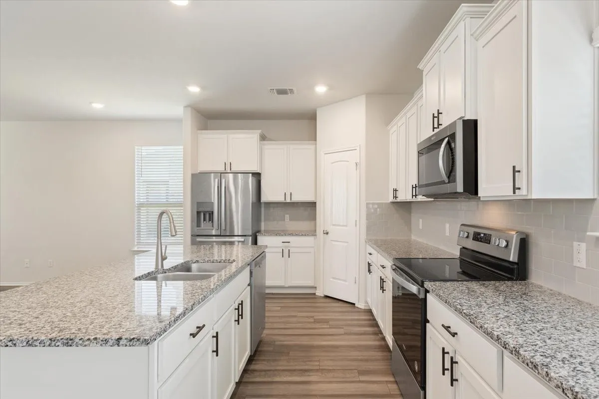 Contemporary kitchen featuring an expansive center island with an undermount sink, granite countertops, white cabinetry, a subway tile backsplash, and stainless steel appliances