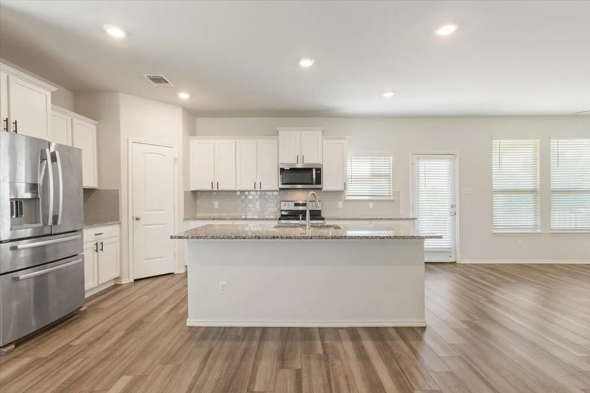 Open-concept kitchen featuring a central island, granite countertops, stainless steel appliances, white cabinetry, and wood-finish flooring