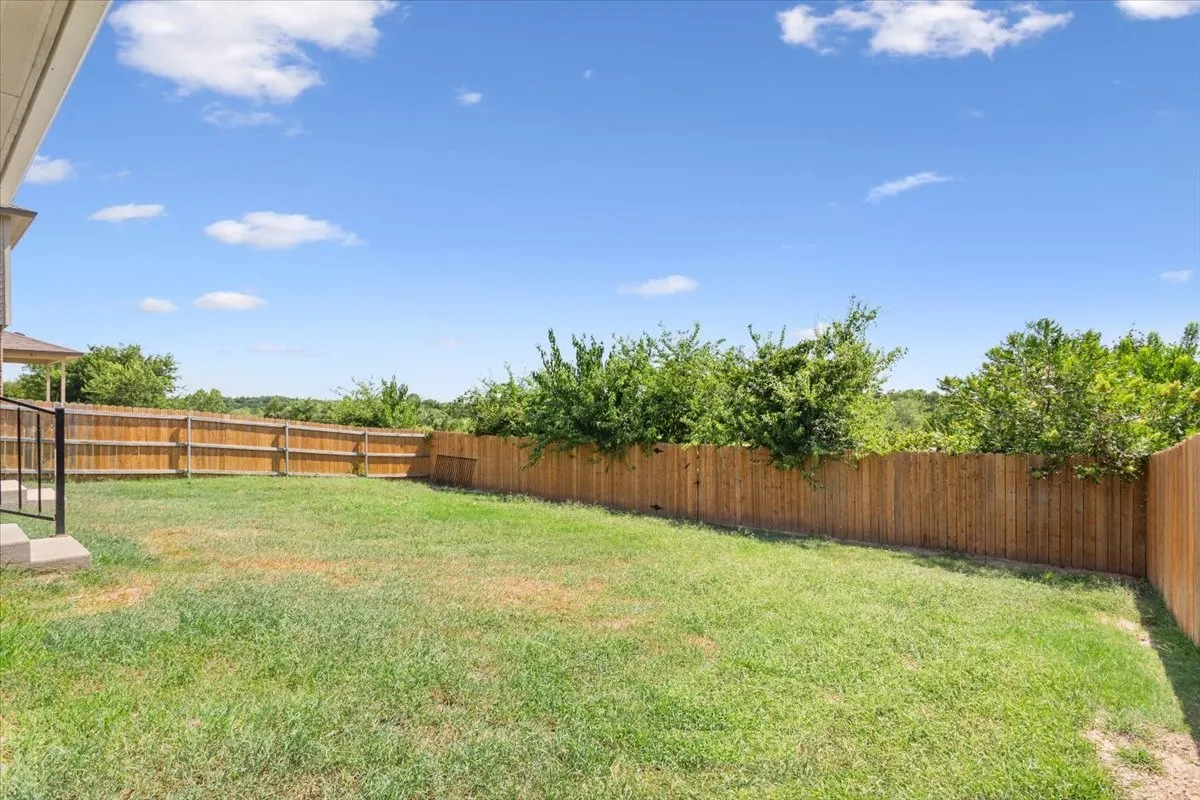 Expansive backyard featuring a privacy fence, green lawn, and mature perimeter trees