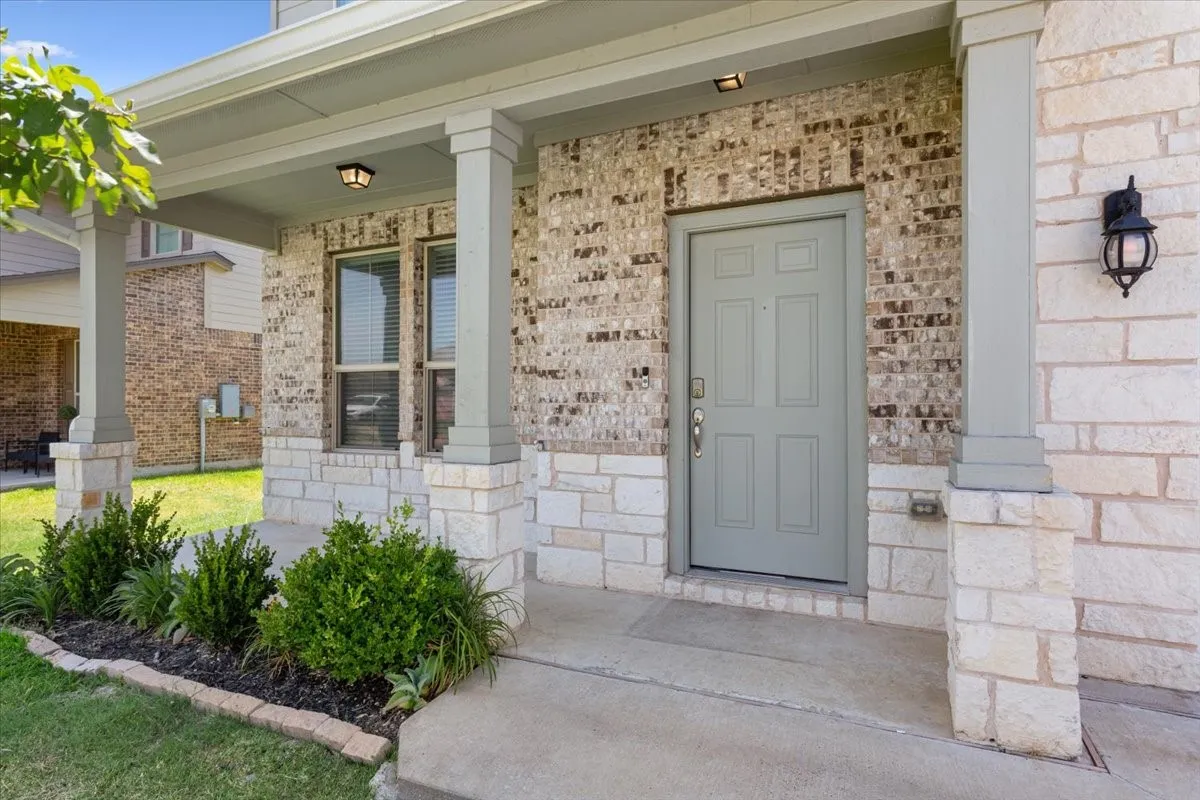 Stone and brick facade with a paneled front door, covered porch, and integrated outdoor lighting