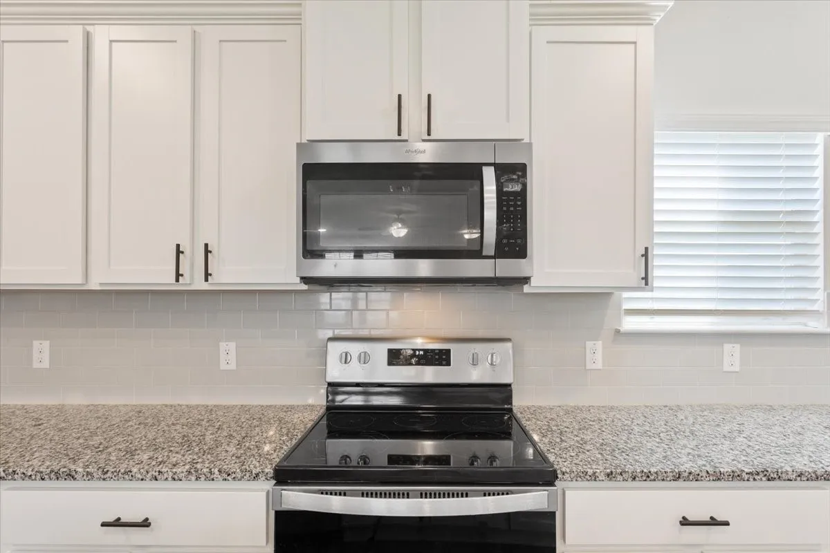 Kitchen featuring stainless steel appliances, white cabinetry, granite countertops, and a subway tile backsplash