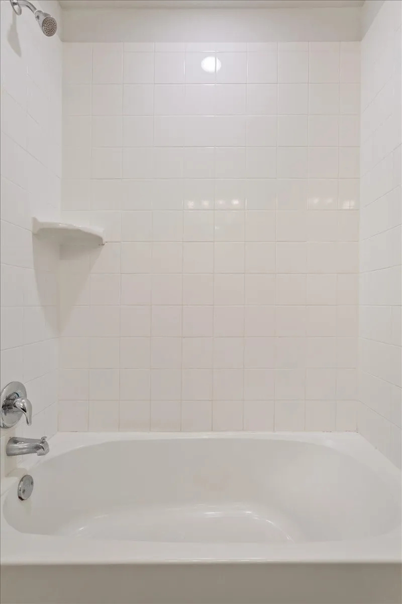 White tiled shower-over-tub with a chrome showerhead, single-handle faucet, and integrated soap dish