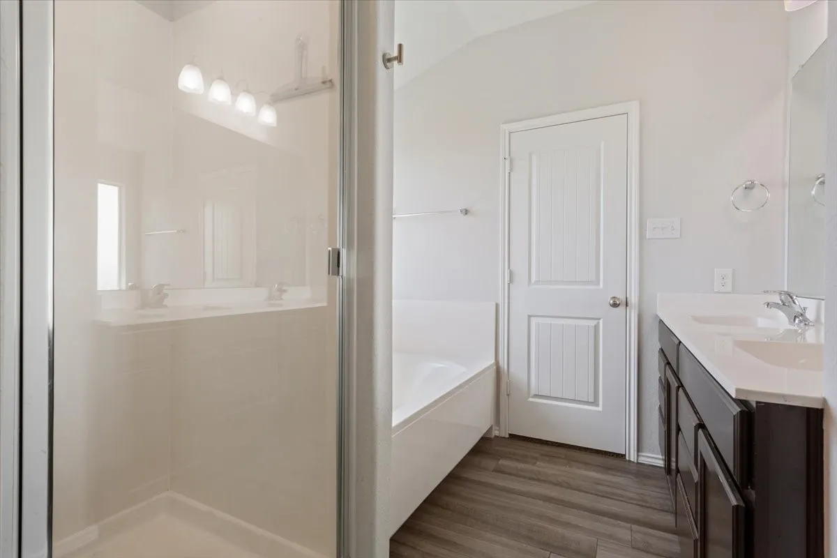 Spacious bathroom featuring a glass-enclosed shower, a separate soaking tub, and a dual-sink vanity with dark cabinetry