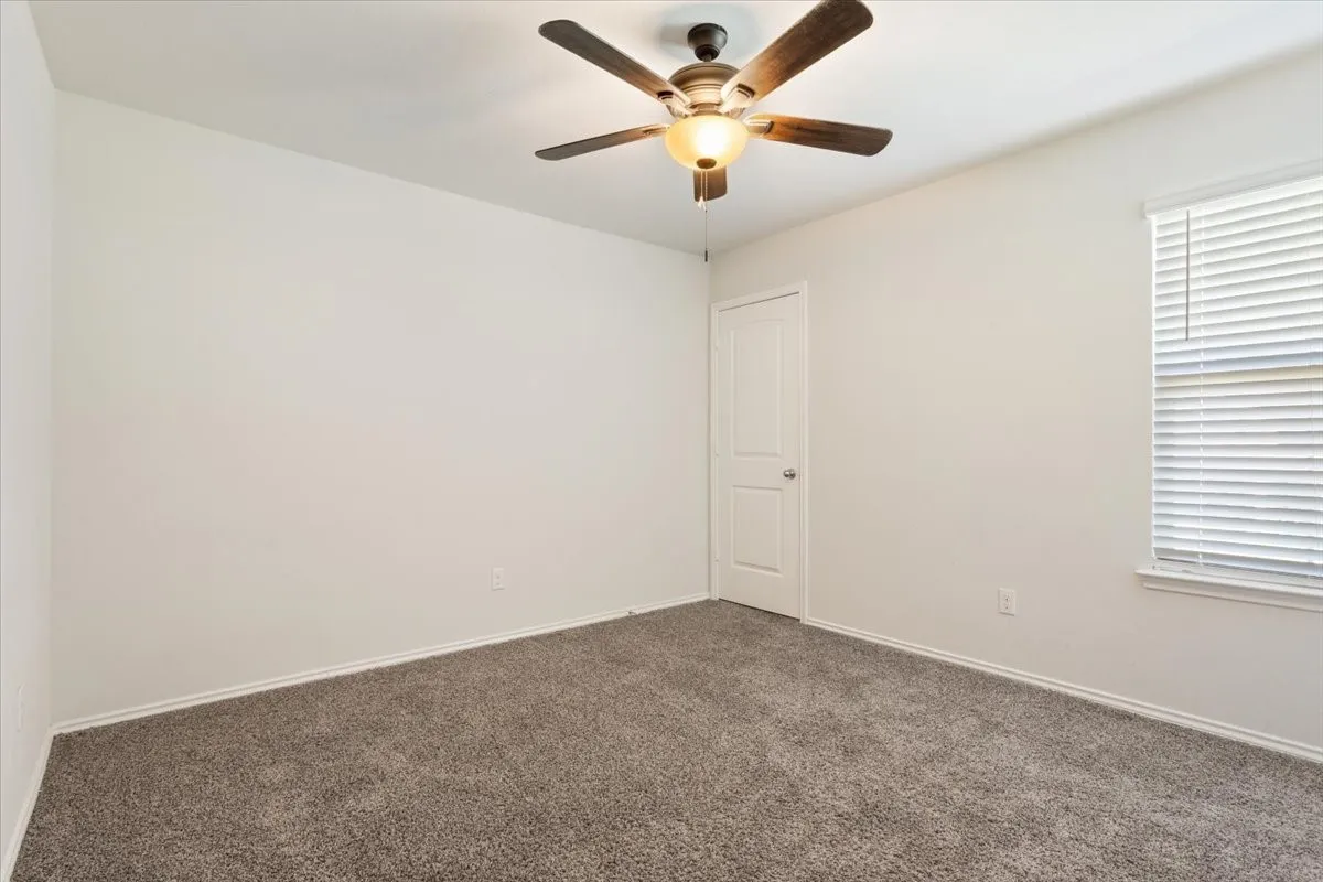 Carpeted room featuring a ceiling fan with integrated lighting, a paneled door, and a window with blinds