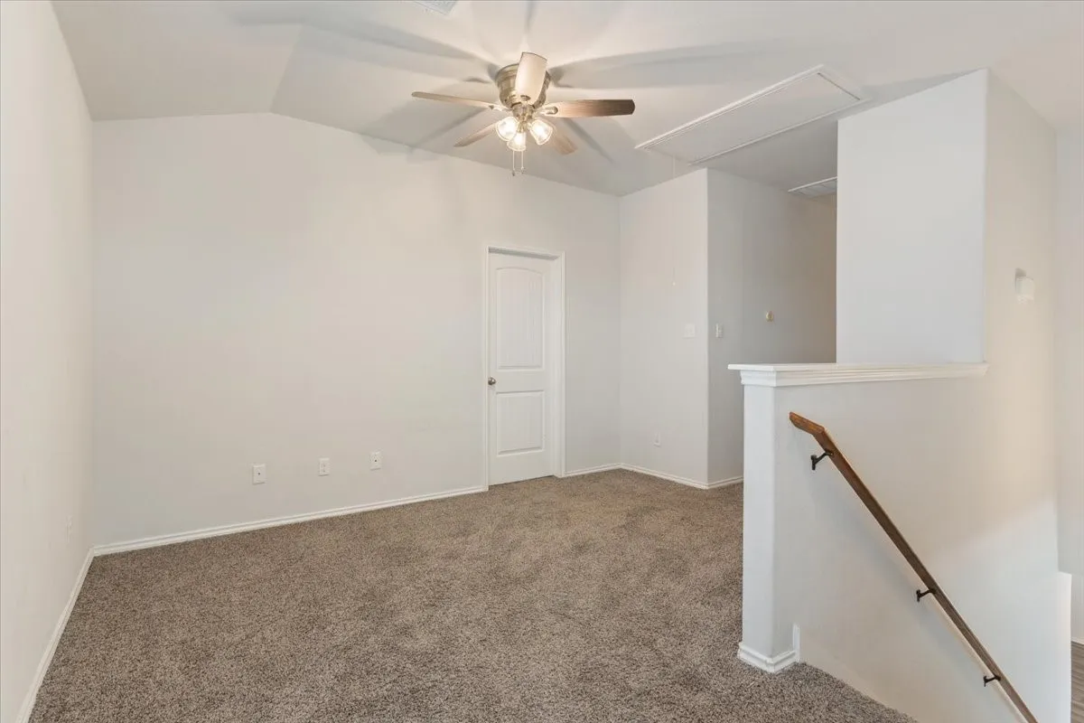 Carpeted room featuring a ceiling fan with light fixture, vaulted ceiling, and a paneled door