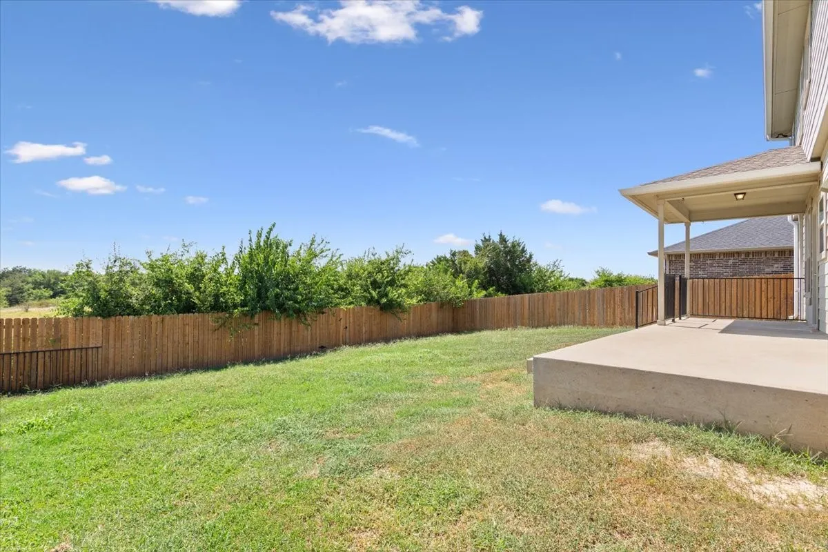 Fenced backyard featuring a covered concrete patio, lush green lawn, and mature perimeter landscaping