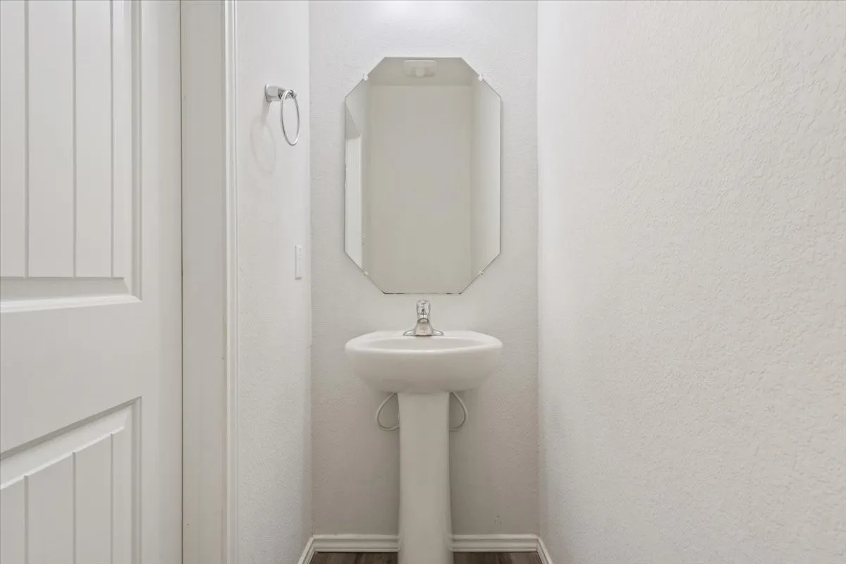 Pedestal sink with chrome faucet, complemented by an octagonal wall mirror