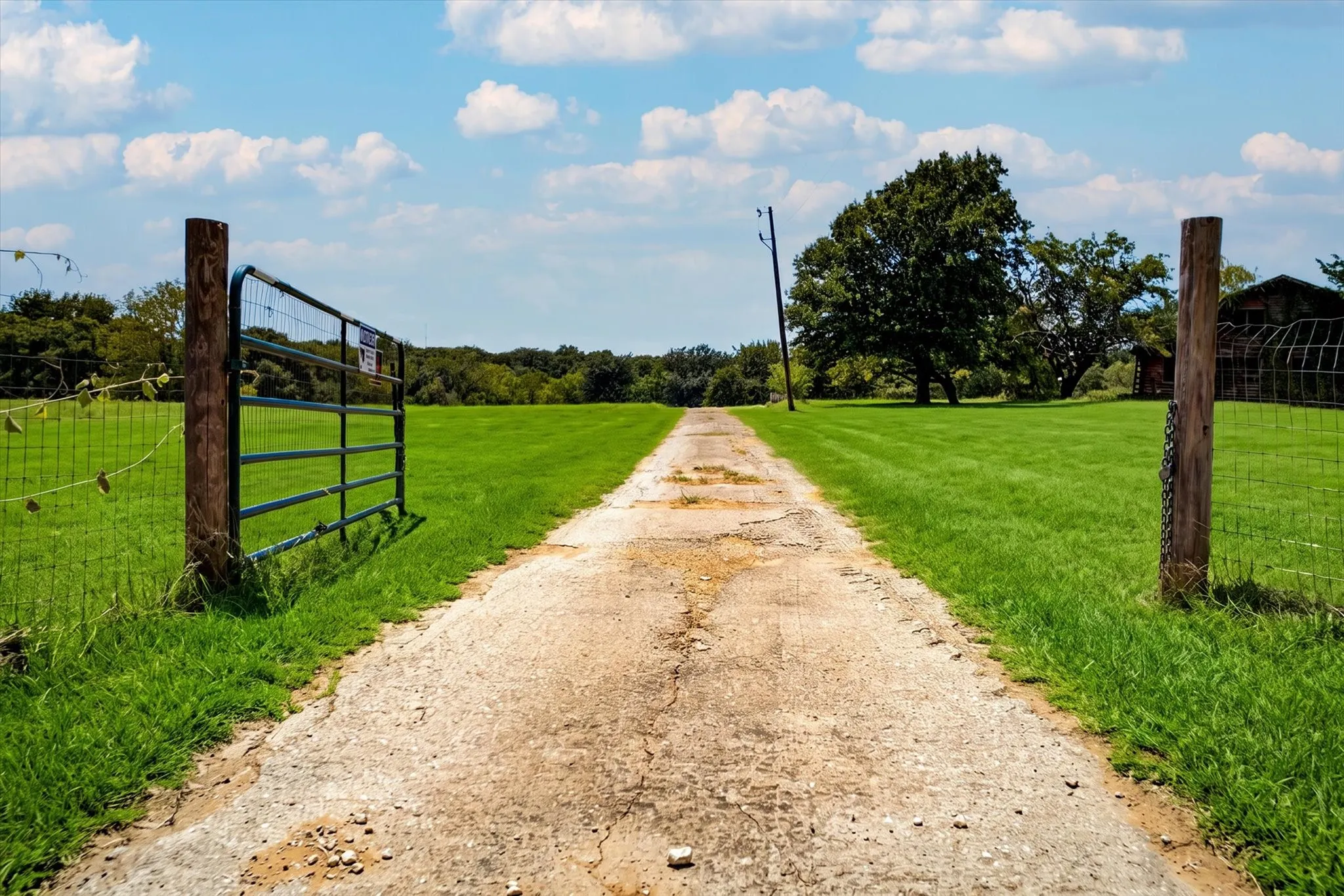 Gravel driveway bordered by manicured green lawns and a metal wire fence