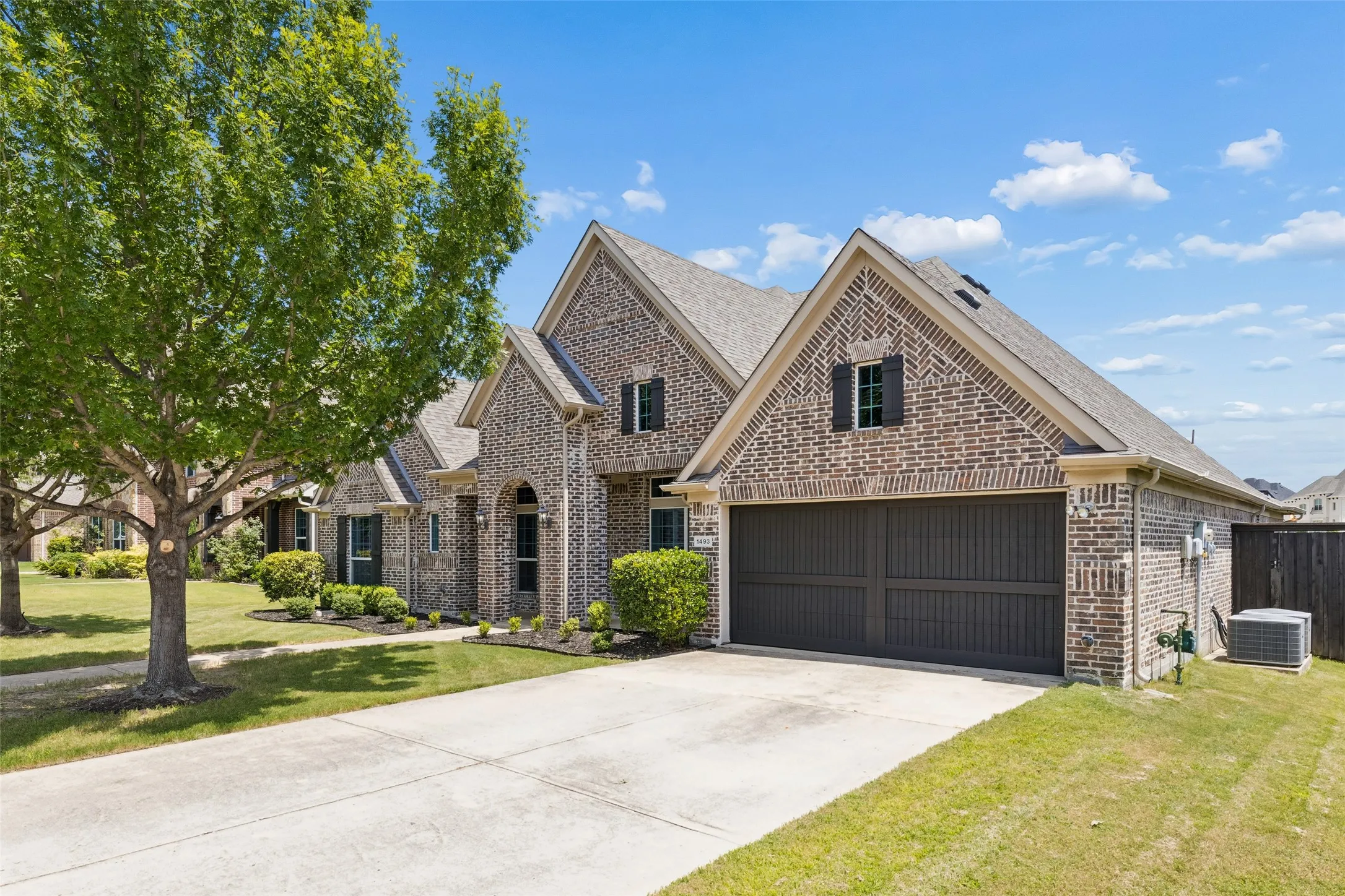 Brick exterior home featuring an attached two-car garage with a dark panel door, a concrete driveway, and mature landscaping