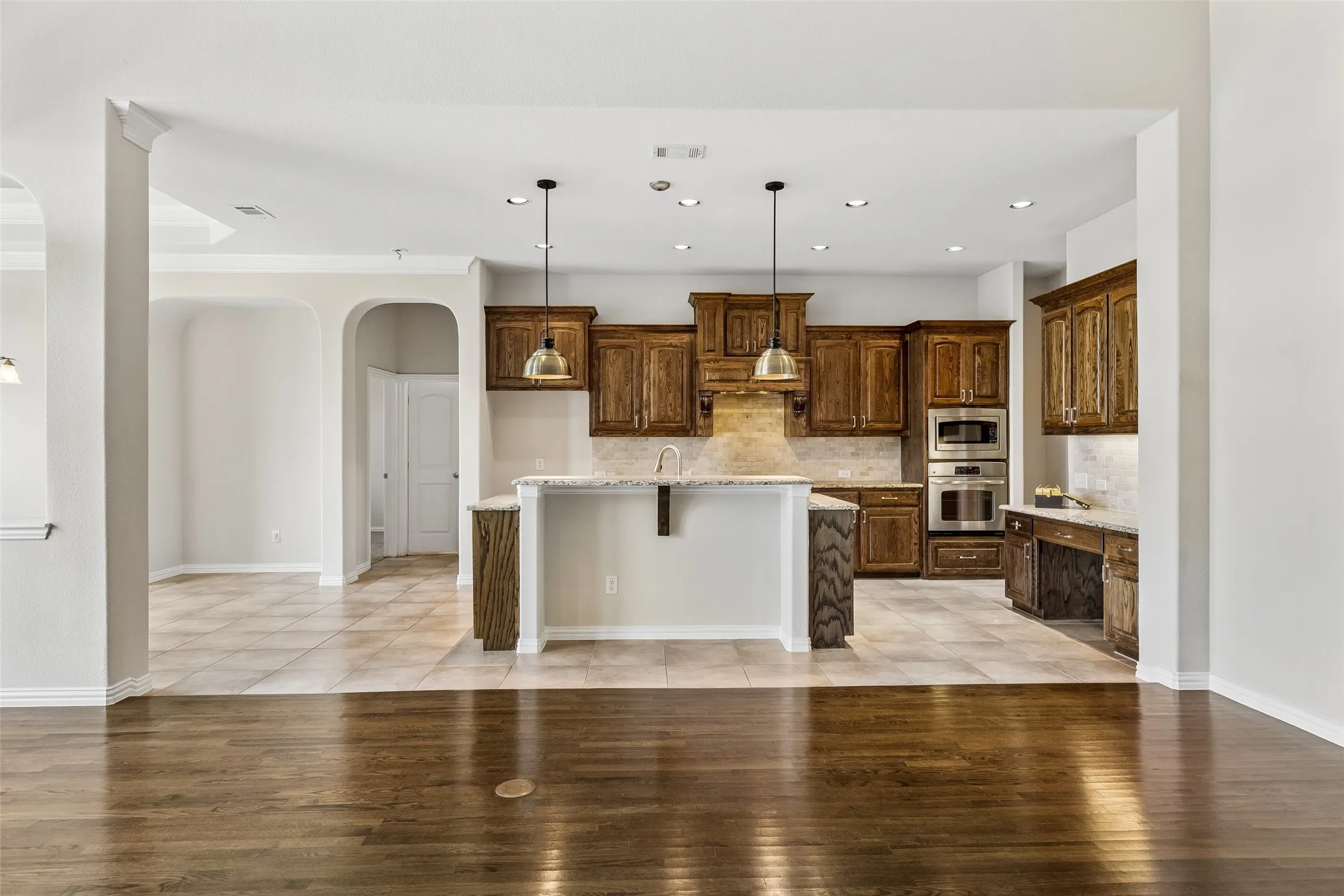 Gourmet kitchen featuring wood cabinetry, stainless steel double ovens, a built-in desk area, recessed lighting, and an island with pendant lighting