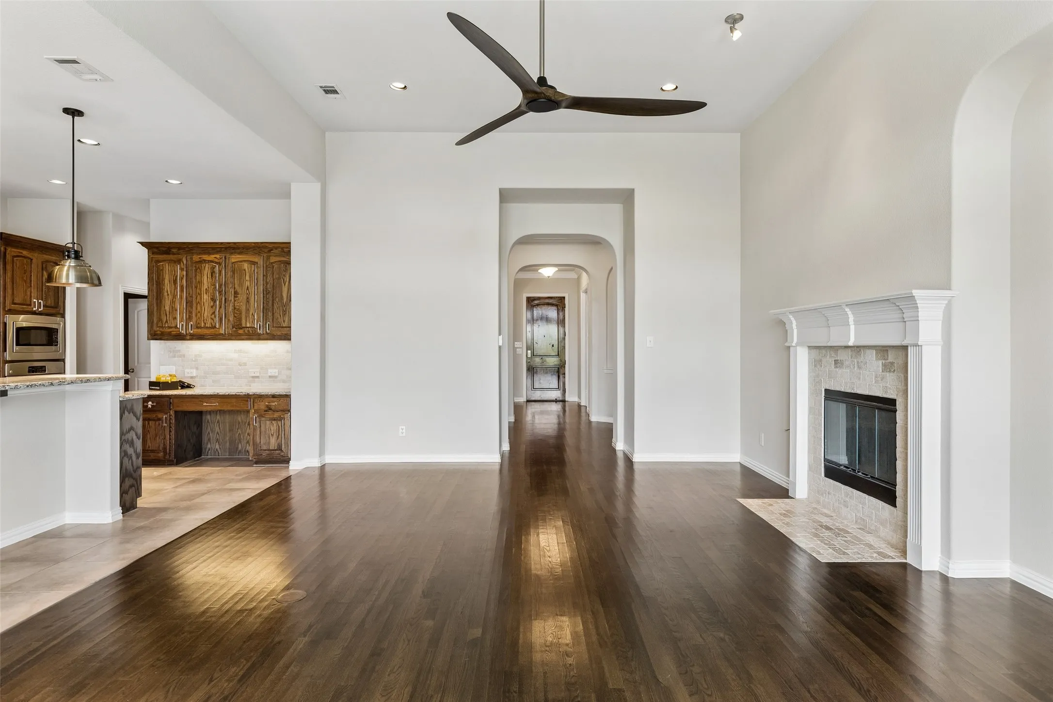 Dark wood-finish flooring extending through an open living area with a fireplace featuring a decorative mantel and stone tile surround