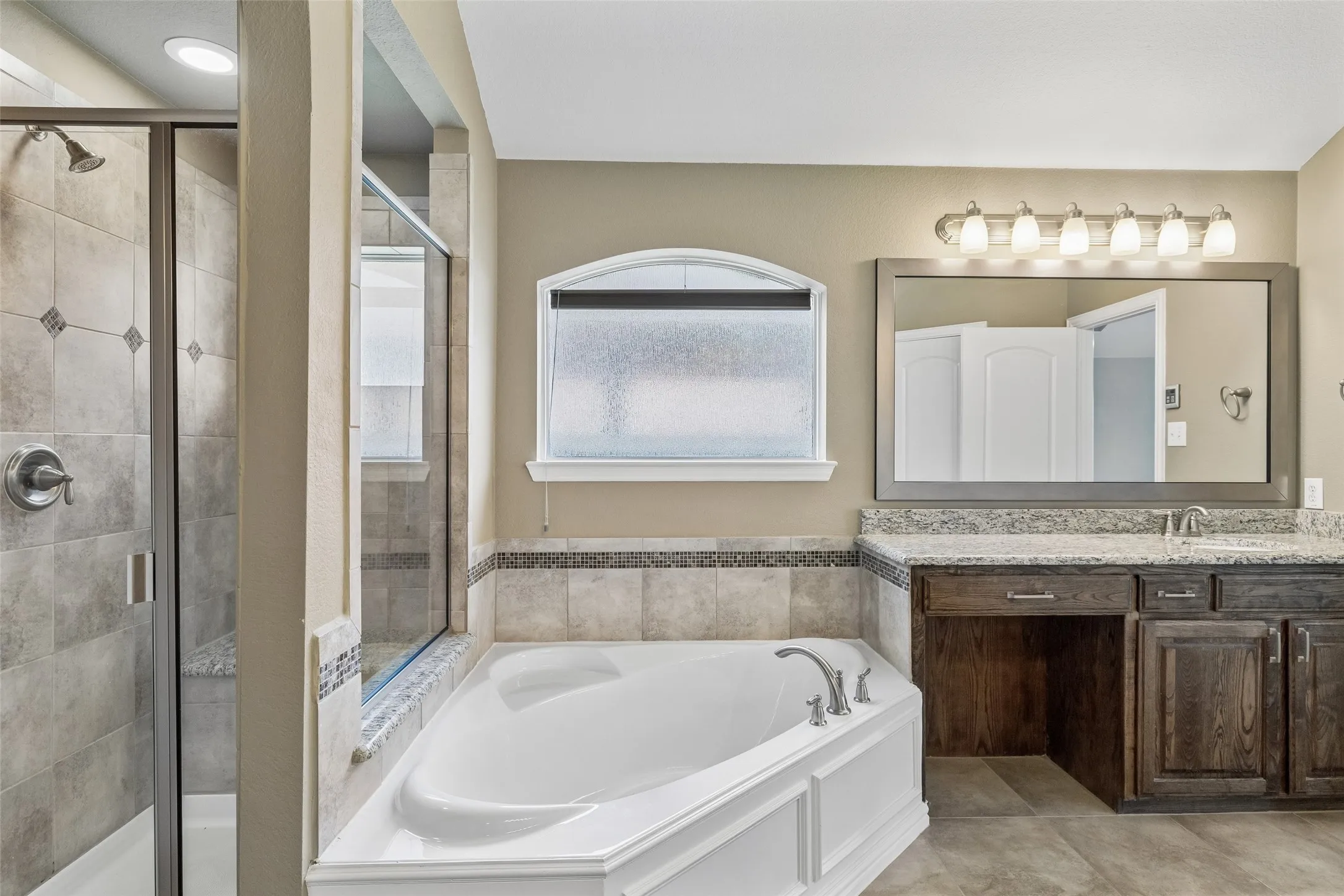 Bathroom featuring a glass-enclosed shower with tile surround, a corner soaking tub, and a dual vanity with a built-in makeup area