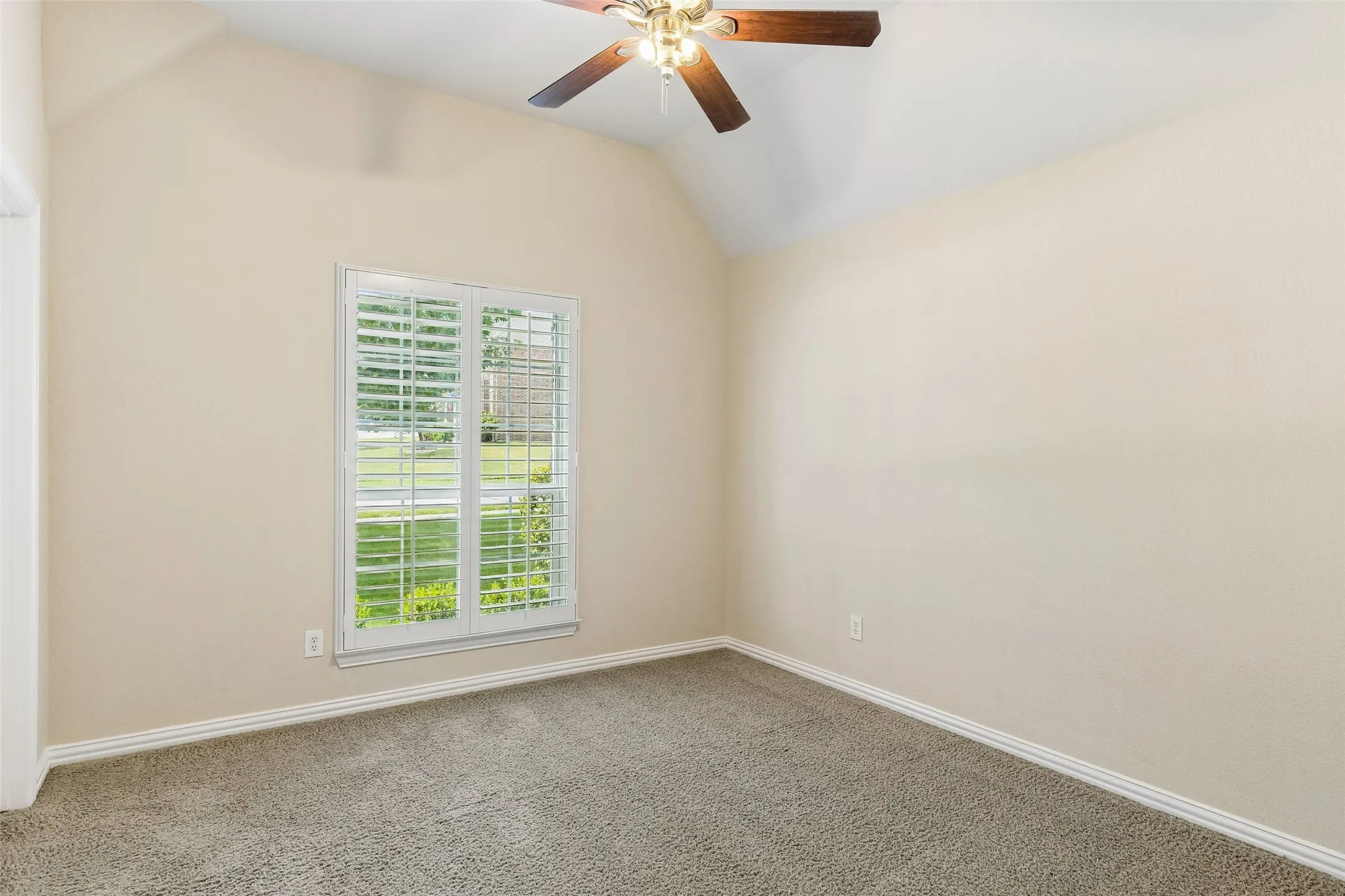Vaulted ceiling room featuring carpet flooring, a ceiling fan with light fixture, and a window with white plantation shutters
