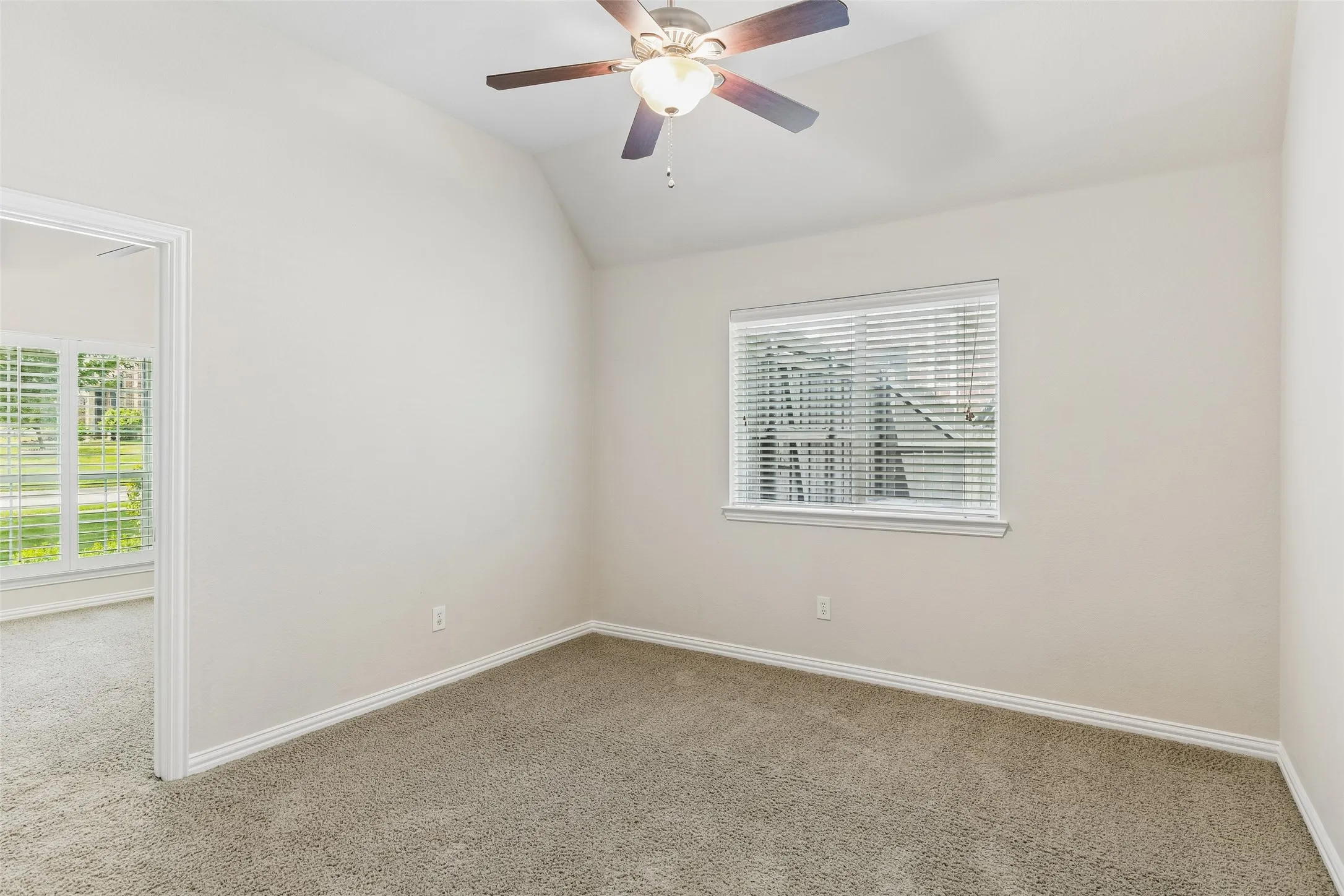 Carpeted room with a vaulted ceiling, a window with blinds, and a ceiling fan with light fixture