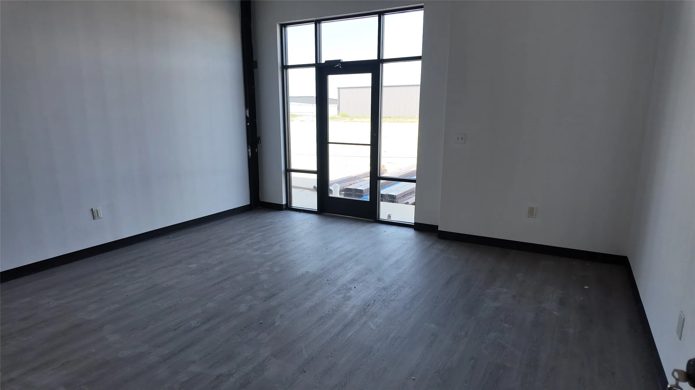 Open concept interior featuring grey wood-finish flooring, white walls, and a large glass entry door