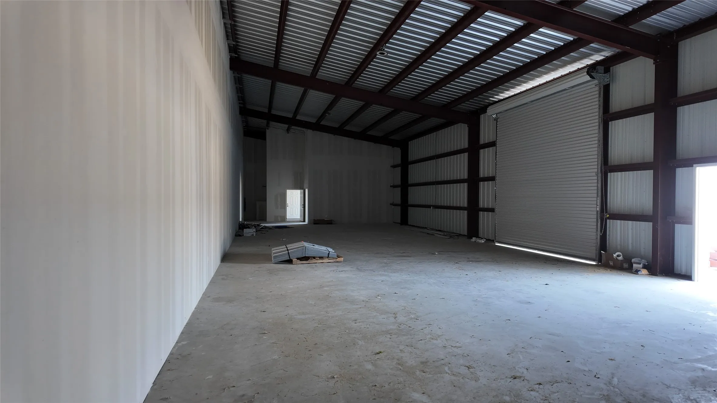 Expansive open interior space with concrete flooring, exposed metal beam construction, and corrugated metal ceiling