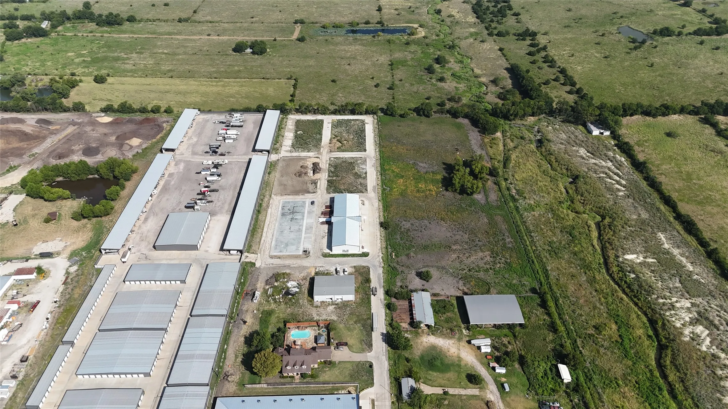 Aerial landscape with numerous industrial-style buildings, open green spaces, and an in-ground swimming pool