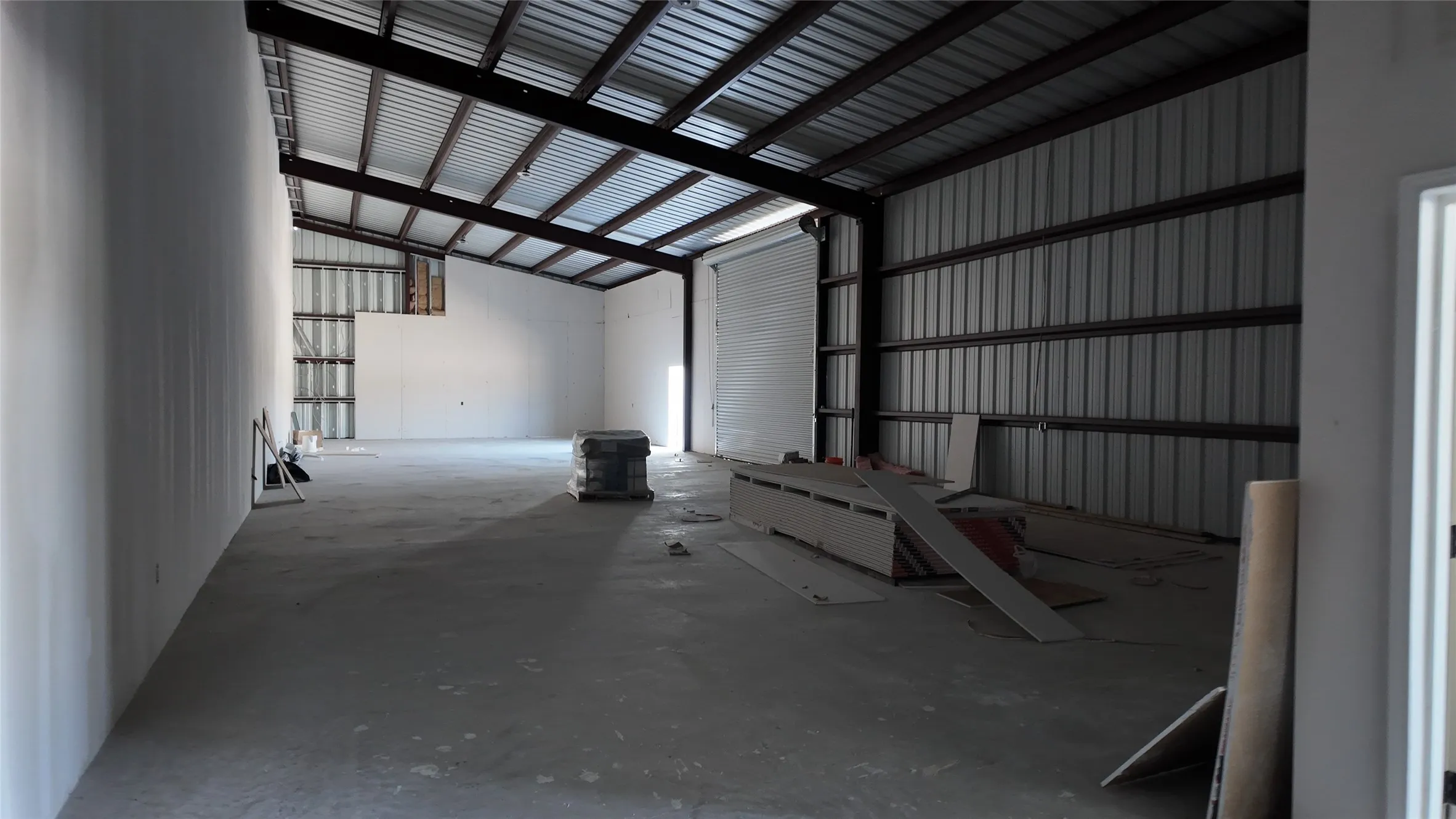 Spacious industrial interior featuring a high-pitched metal roof, exposed structural beams, and concrete flooring