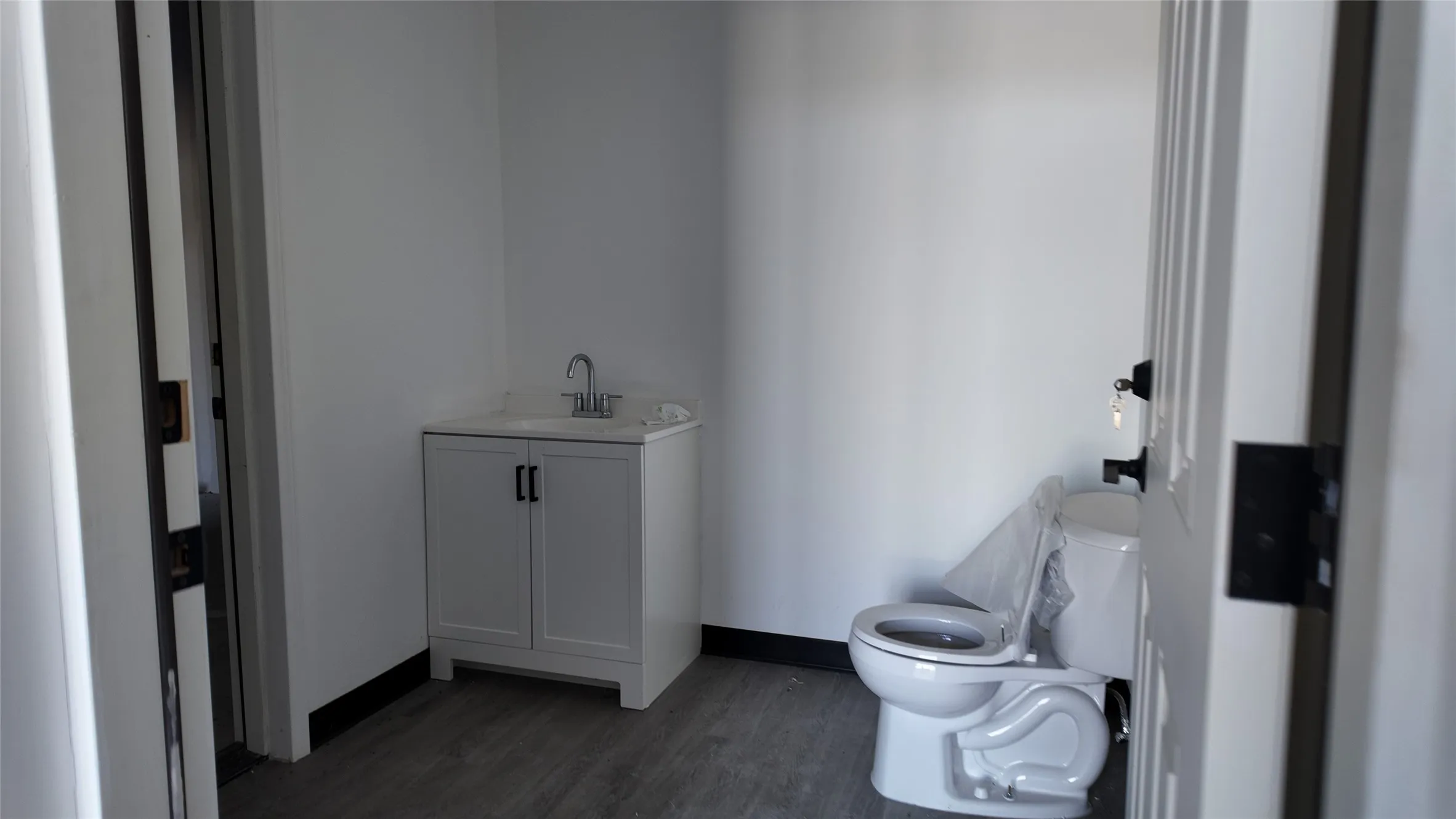 Bathroom with wood-finish flooring, white walls, and dark trim