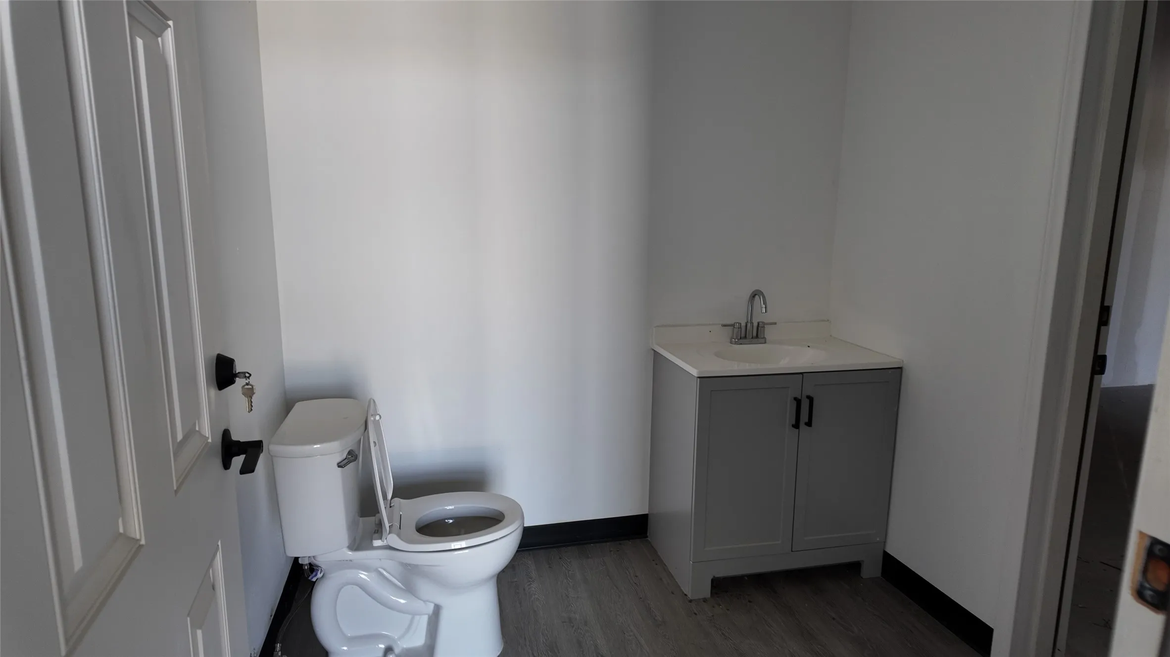 Contemporary powder room featuring a gray vanity with an integrated sink, a single-handle faucet, and plank-style flooring