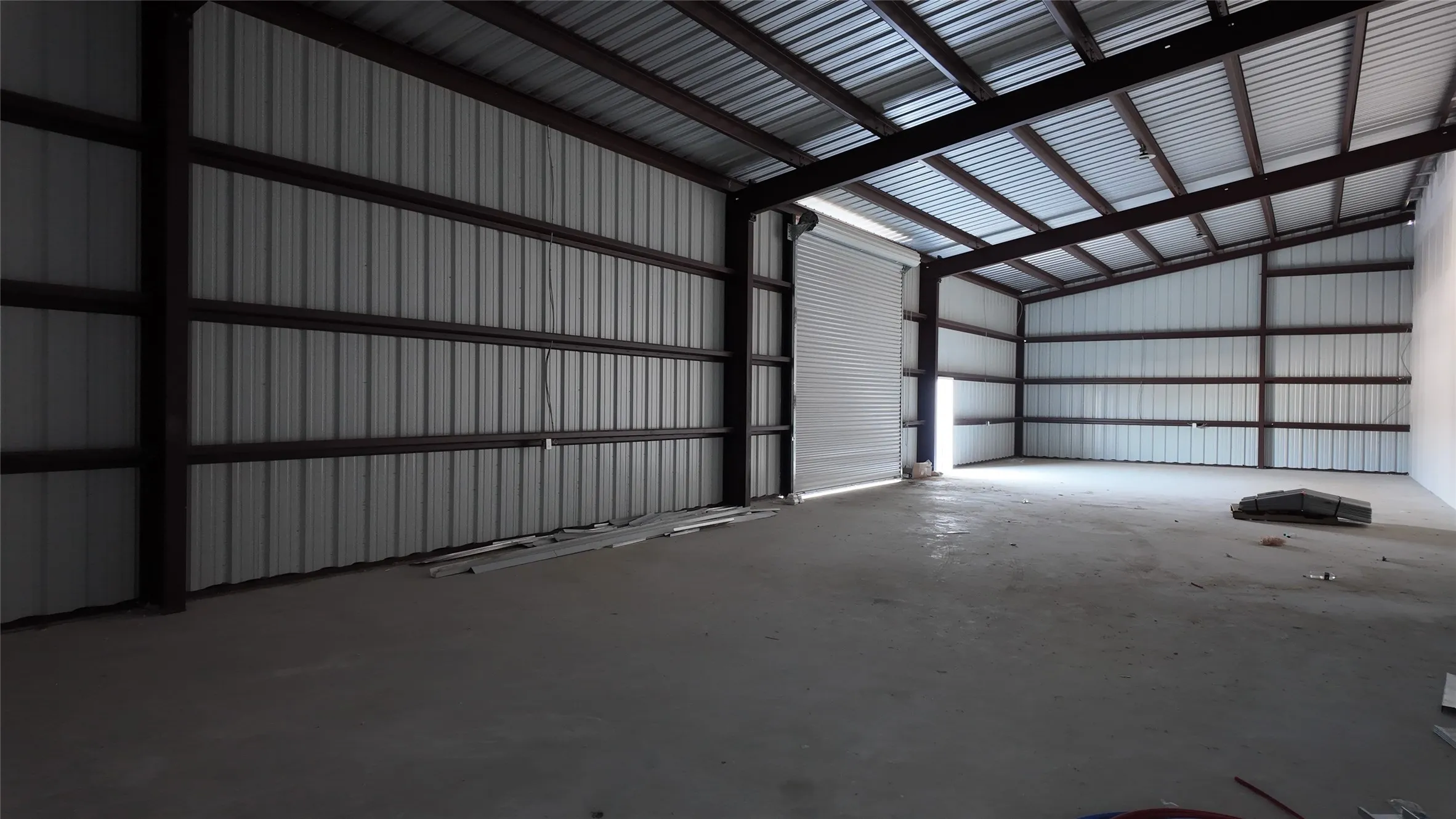 Spacious interior featuring a concrete floor, corrugated metal walls, exposed structural beams, and a large roll-up door