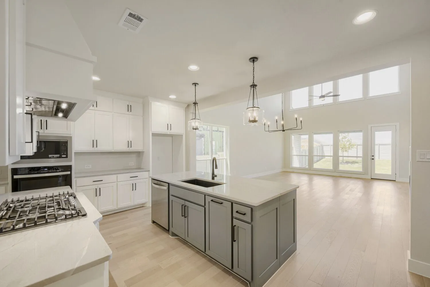 Open-concept kitchen and living area featuring a large center island with a sink, stainless steel appliances, white cabinetry, and light wood-finish flooring
