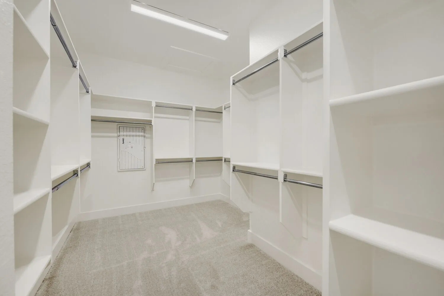 Spacious walk-in closet featuring white built-in shelving, multiple hanging rods, and light gray carpeting