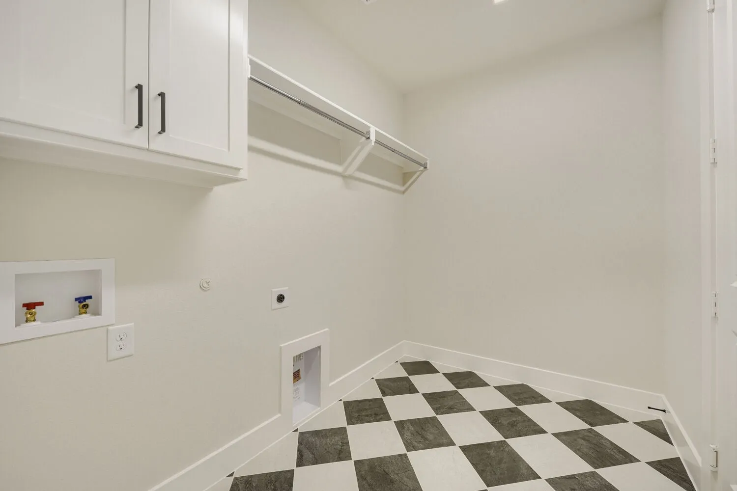 Utility room featuring checkerboard tile flooring, white shaker cabinetry with dark hardware, a built-in hanging rod, and dedicated appliance hookups