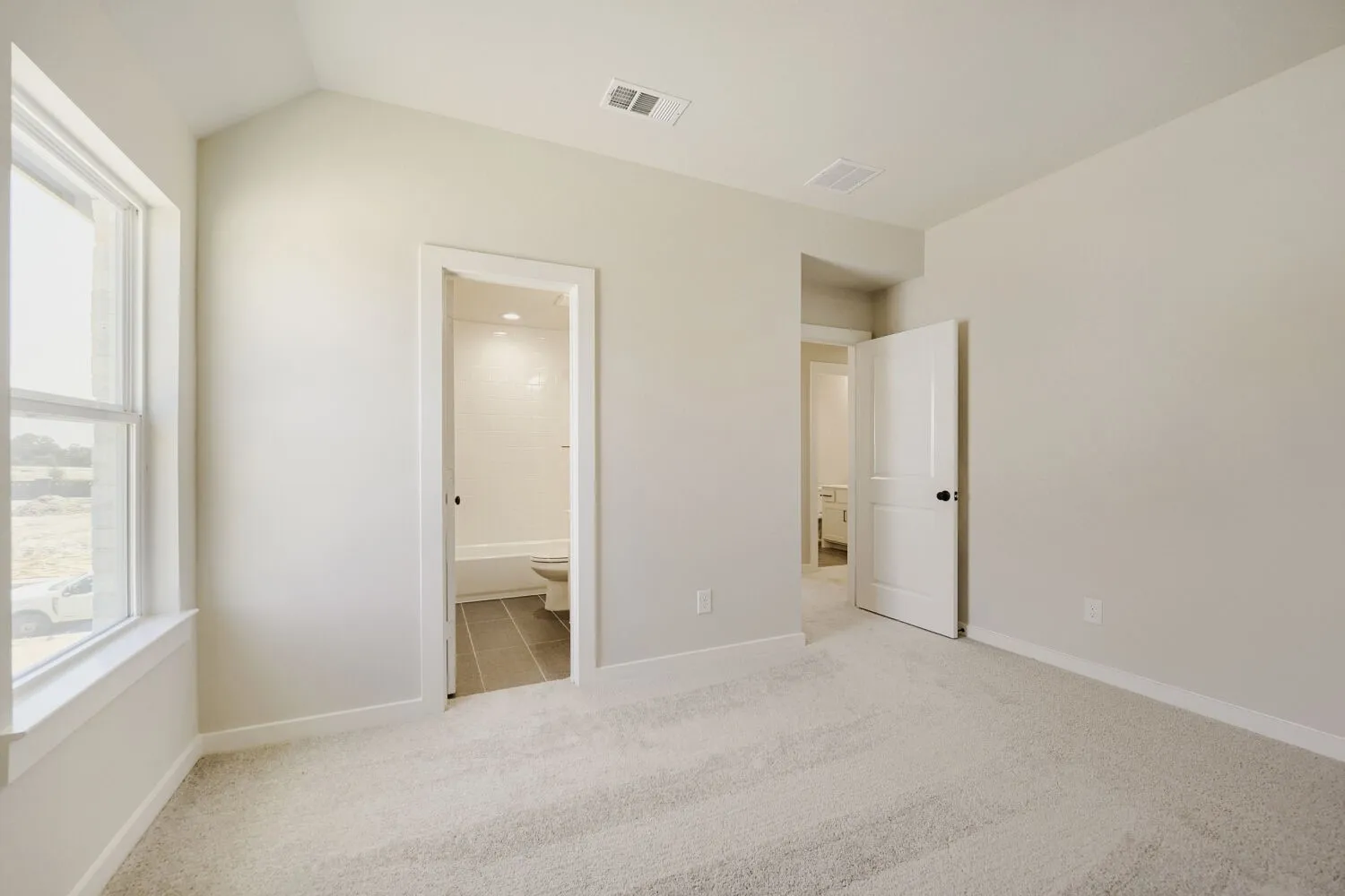 Carpeted room featuring a window with white trim, a vaulted ceiling, and two doorways