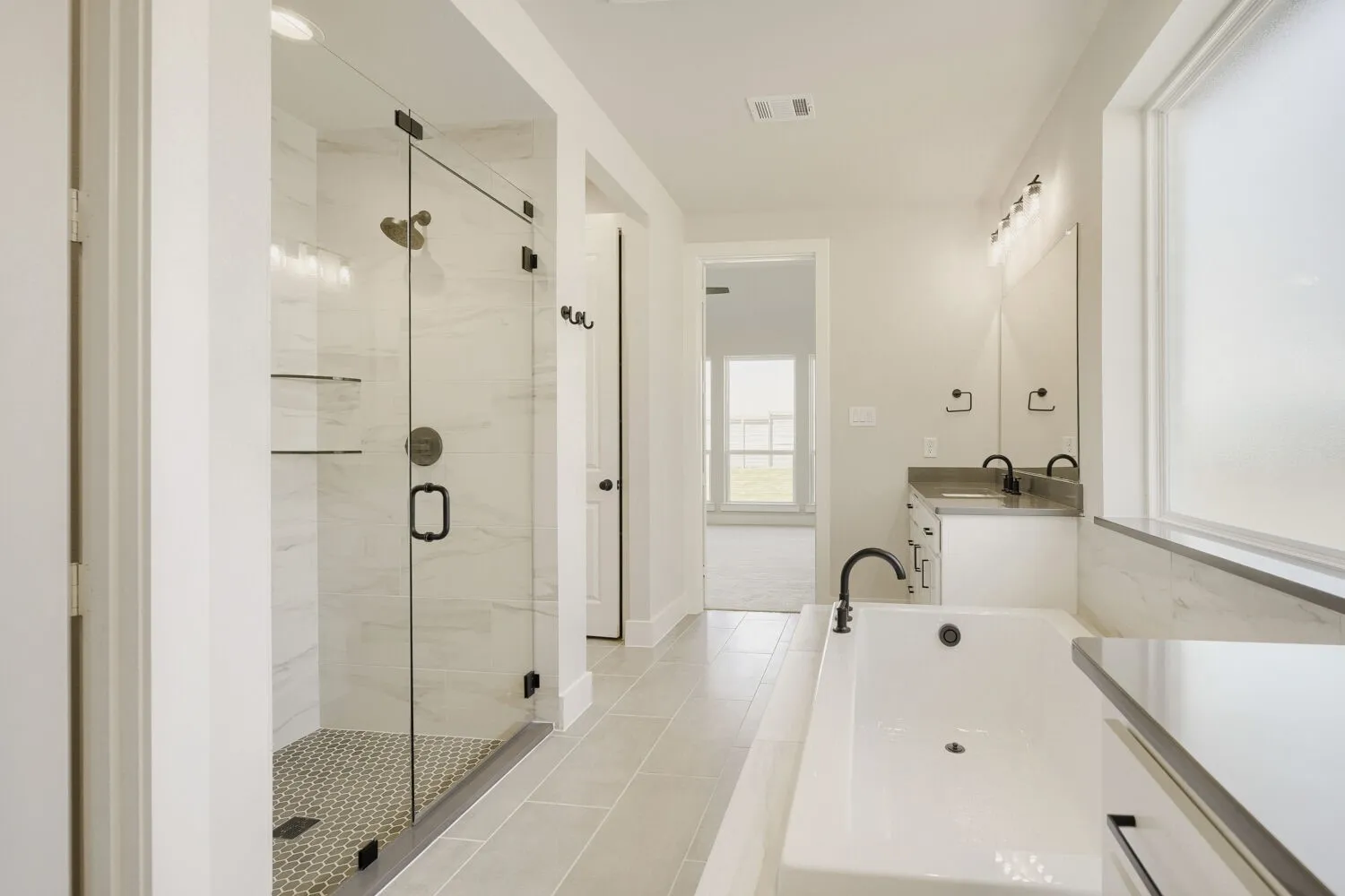 Modern main bathroom featuring a glass-enclosed shower with honeycomb tile flooring, a soaking tub with black fixtures, and a dual-sink vanity with a dark countertop