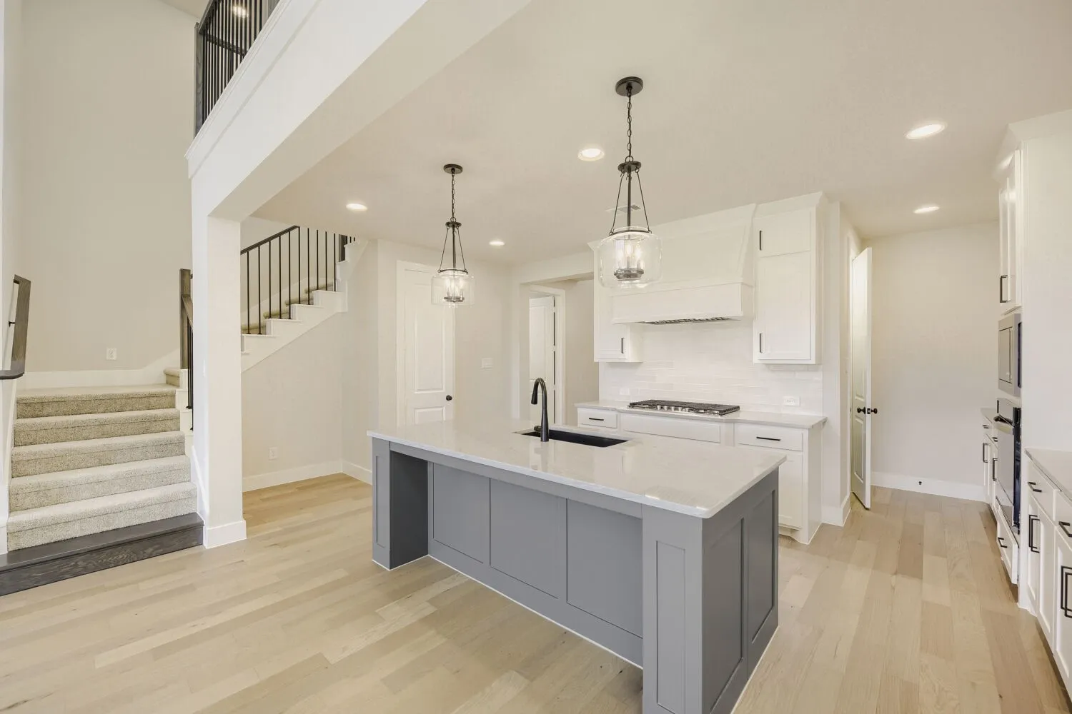 Open-concept kitchen featuring a large island with a light-toned countertop, white cabinetry, a built-in range, and a subway tile backsplash