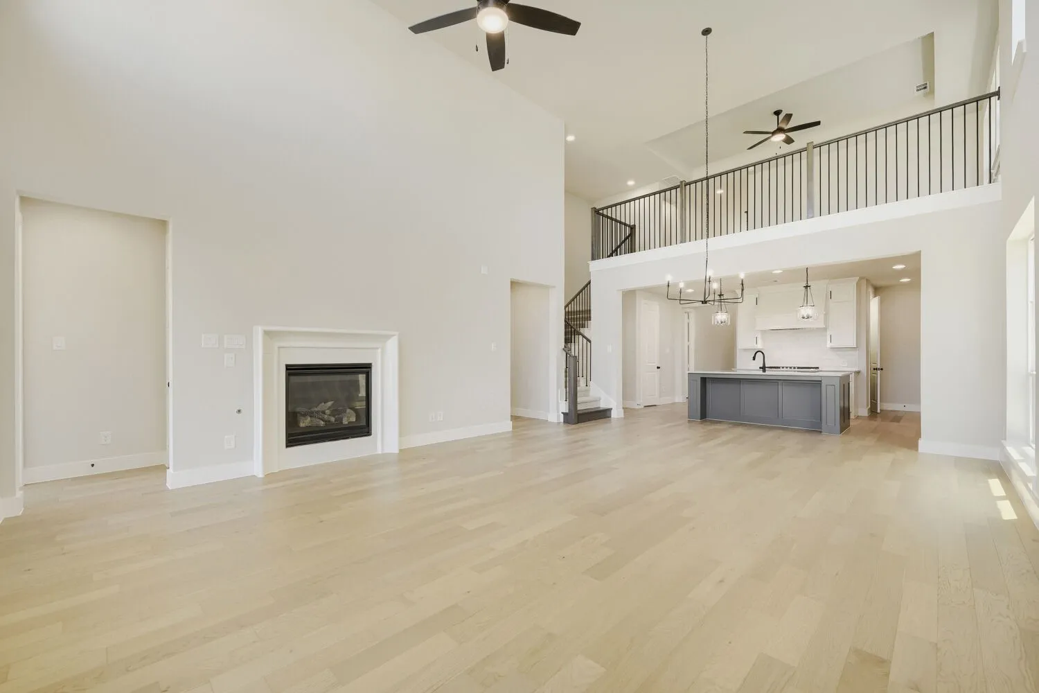 Spacious living area featuring high ceilings, light wood-finish flooring, and a fireplace with a classic mantel