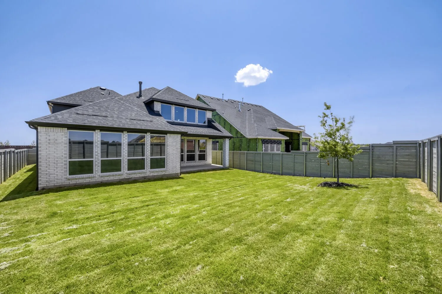 Expansive green lawn surrounds the rear of the property, featuring a light brick exterior with multiple large windows