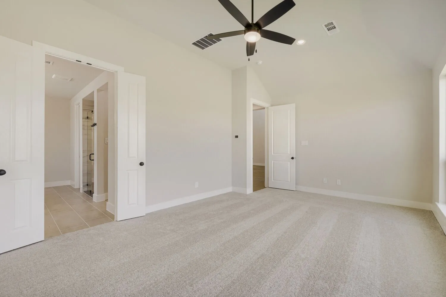 Spacious main Bedroom featuring vaulted ceilings, light gray carpet, and a modern black ceiling fan with integrated lighting