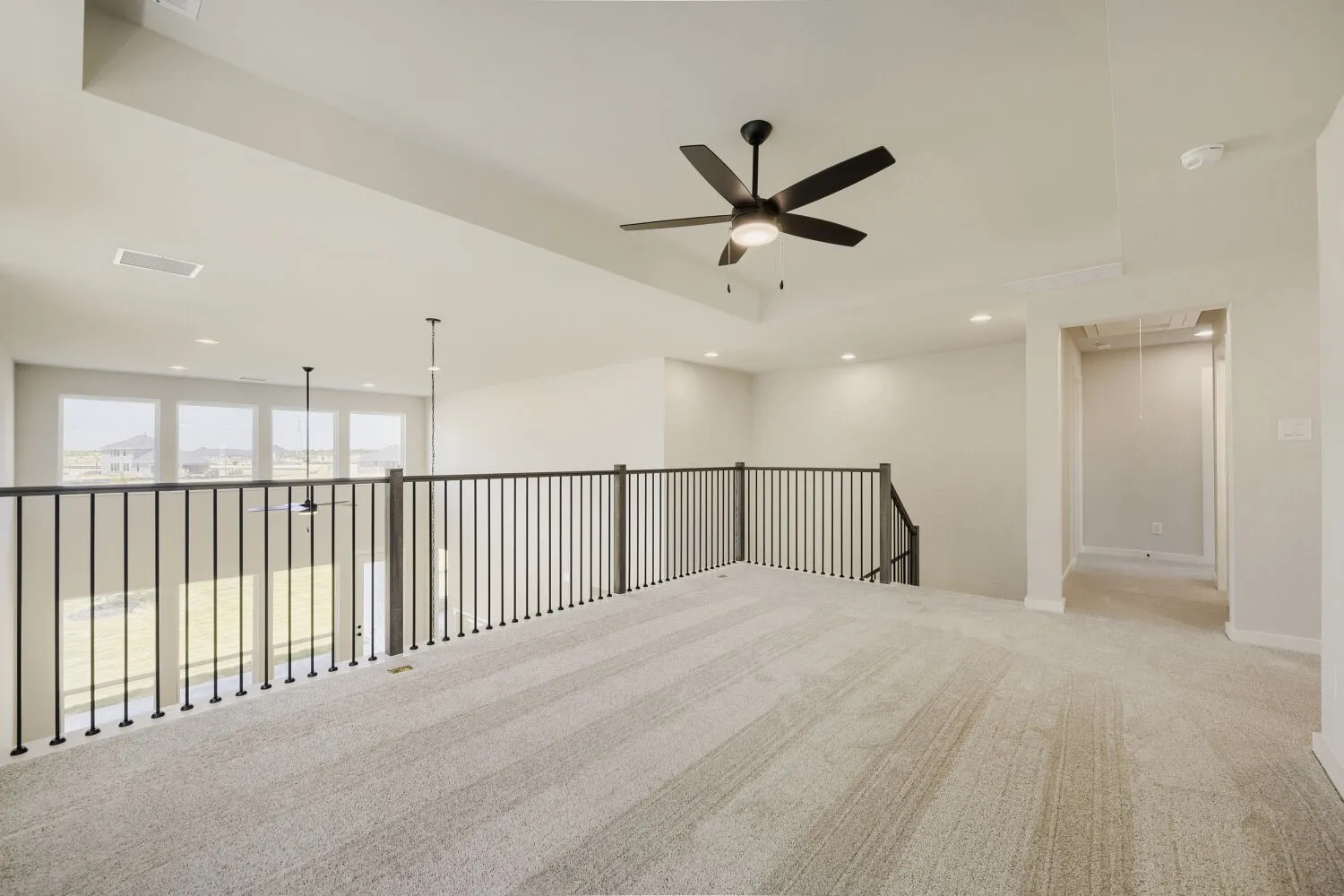Spacious upstairs loft featuring light-toned carpet, a modern ceiling fan, recessed lighting, and a black metal spindle railing