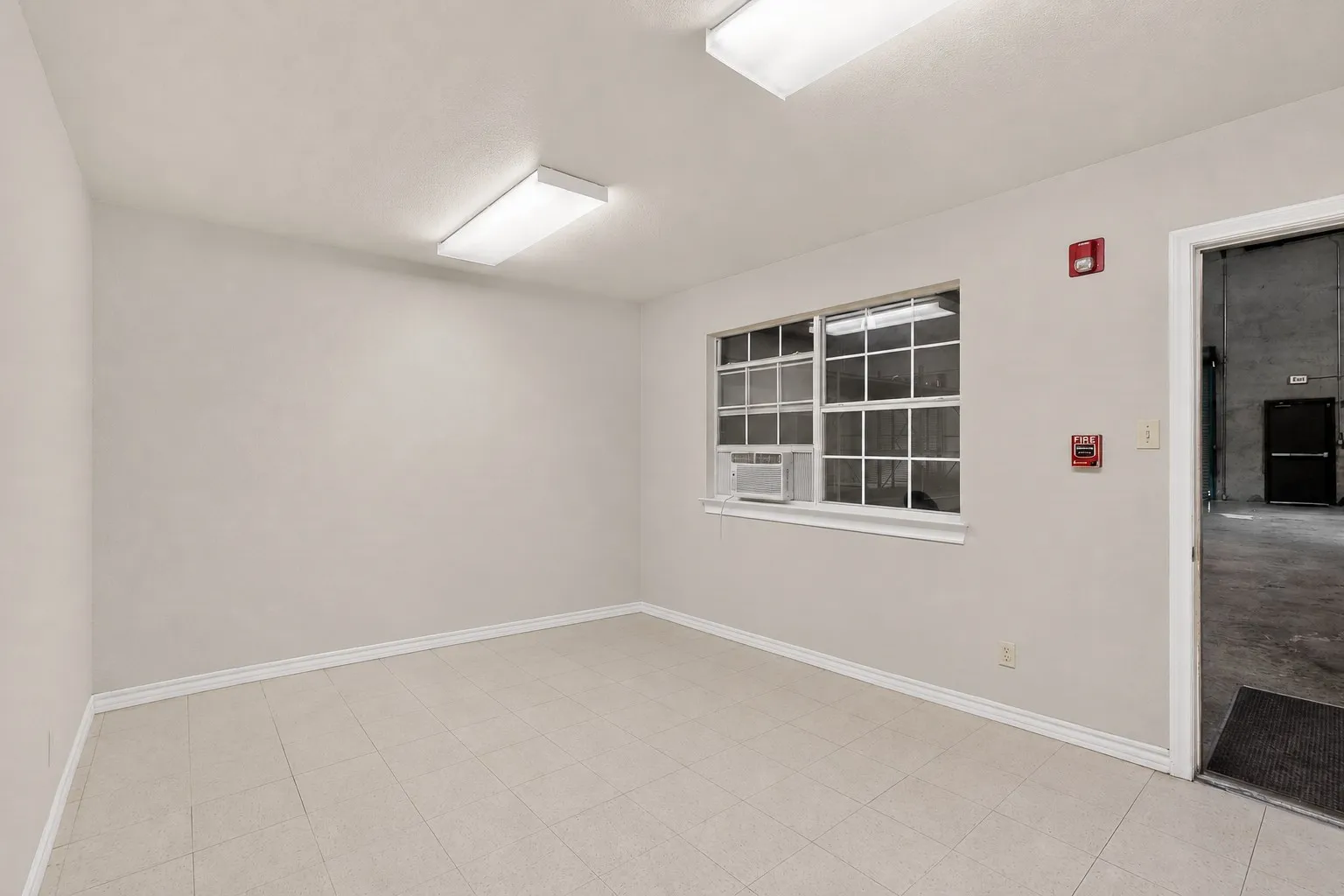 Neutral tone wall finishes, tiled flooring, window with gridded panes, and overhead fluorescent lighting fixtures