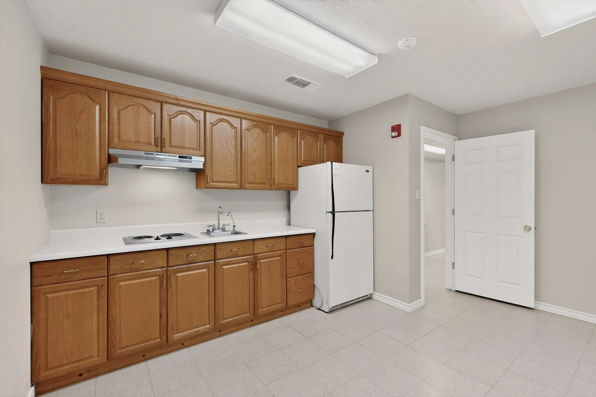 Kitchenette with wood cabinetry, white countertops, a built-in cooktop, and a refrigerator